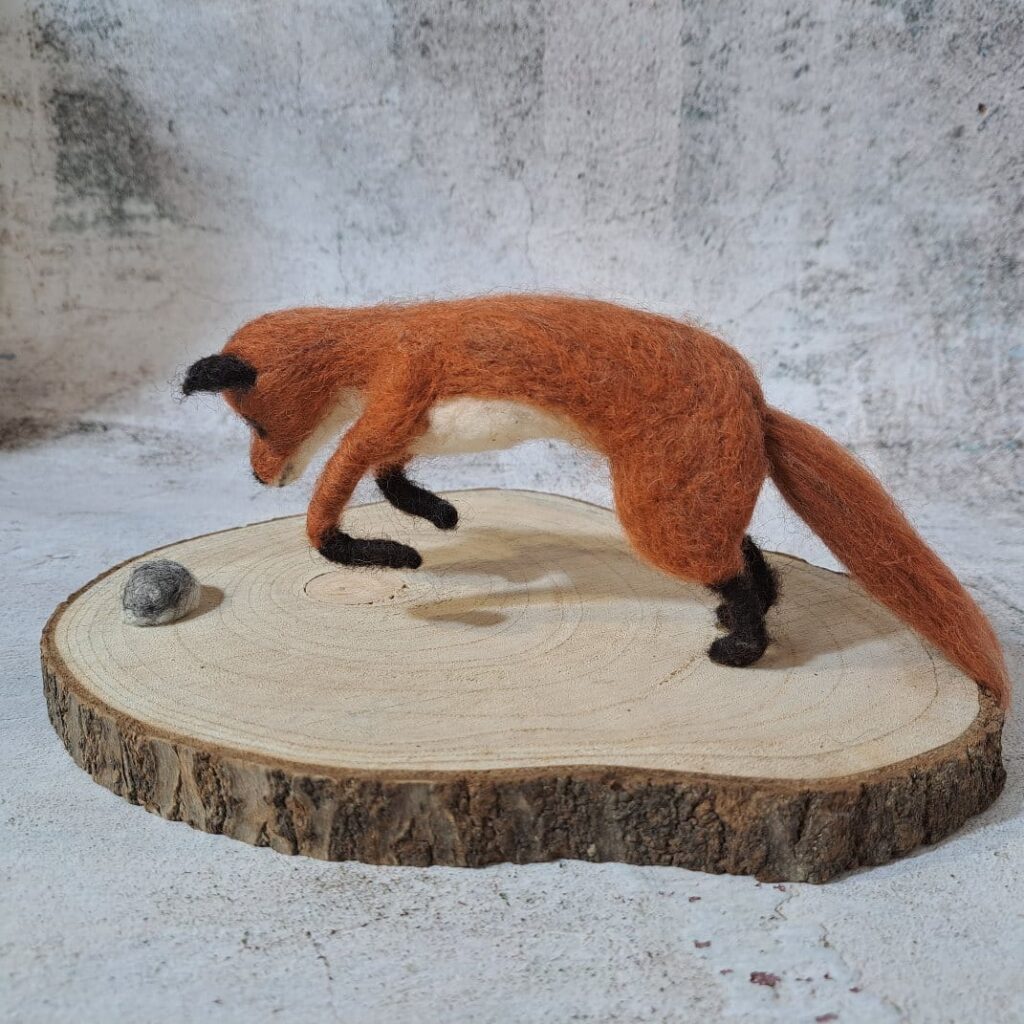 Escultura zorro de fieltro cazando erizo sobre base de madera natural
